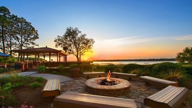 A gazebo, a fire pit, and wooden benches in a garden setting with a view of the sunset over a body of water. - Enjoyable 2-bedroom hotel in Hilton Head Island with WiFi (Hilton Head Island)