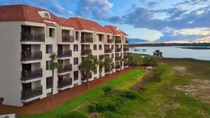 A multi-story hotel with balconies, a grassy area, and a view of the water. - Enjoyable 2-bedroom hotel in Hilton Head Island with WiFi (Hilton Head Island)