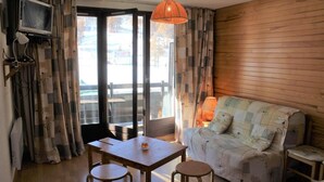 A cozy room with a wooden wall, a sofa, a table with two stools, a TV on a stand, and a window with curtains. - 10m from ski slopes, 1st floor, view ski slopes, balcony, tv, ski locker, 30m², Risoul (Risoul)