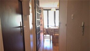 A narrow hallway with wooden flooring leading to a room with a window and a table. - 10m from ski slopes, 1st floor, view ski slopes, balcony, tv, ski locker, 30m², Risoul (Risoul)