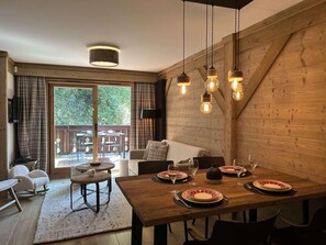 Un coin repas avec une table en bois dressée pour quatre personnes, un canapé et une vue sur l’extérieur.