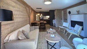 Ein modernes Wohnzimmer mit Sofa, Couchtisch und Sesseln, ein Essbereich mit Tisch und Stühlen sowie ein Kamin.