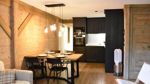 Ein gemütlicher, gut beleuchteter Essbereich mit einem Holztisch für vier Personen, an dessen Seite dunkle Holzschränke stehen und im Hintergrund eine moderne Küche erkennbar ist.