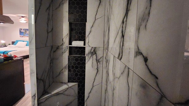A bathroom with marble walls, a shower area, and a shelf with a towel.