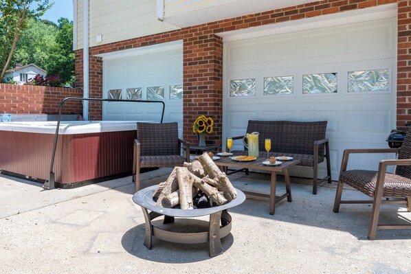 Ein Außenbereich mit Terrasse, Whirlpool, Feuerstelle, Korbmöbeln und einer Garagentür mit Milchglasfenstern.