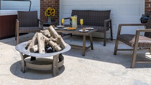 An outdoor patio with a hot tub, wicker furniture, and a fire pit.
