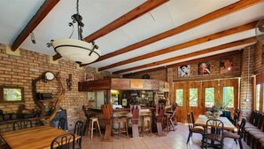 A rustic dining area with wooden tables and chairs, a bar counter, and a brick wall. - Mukurumanzi Lodge (Polokwane)