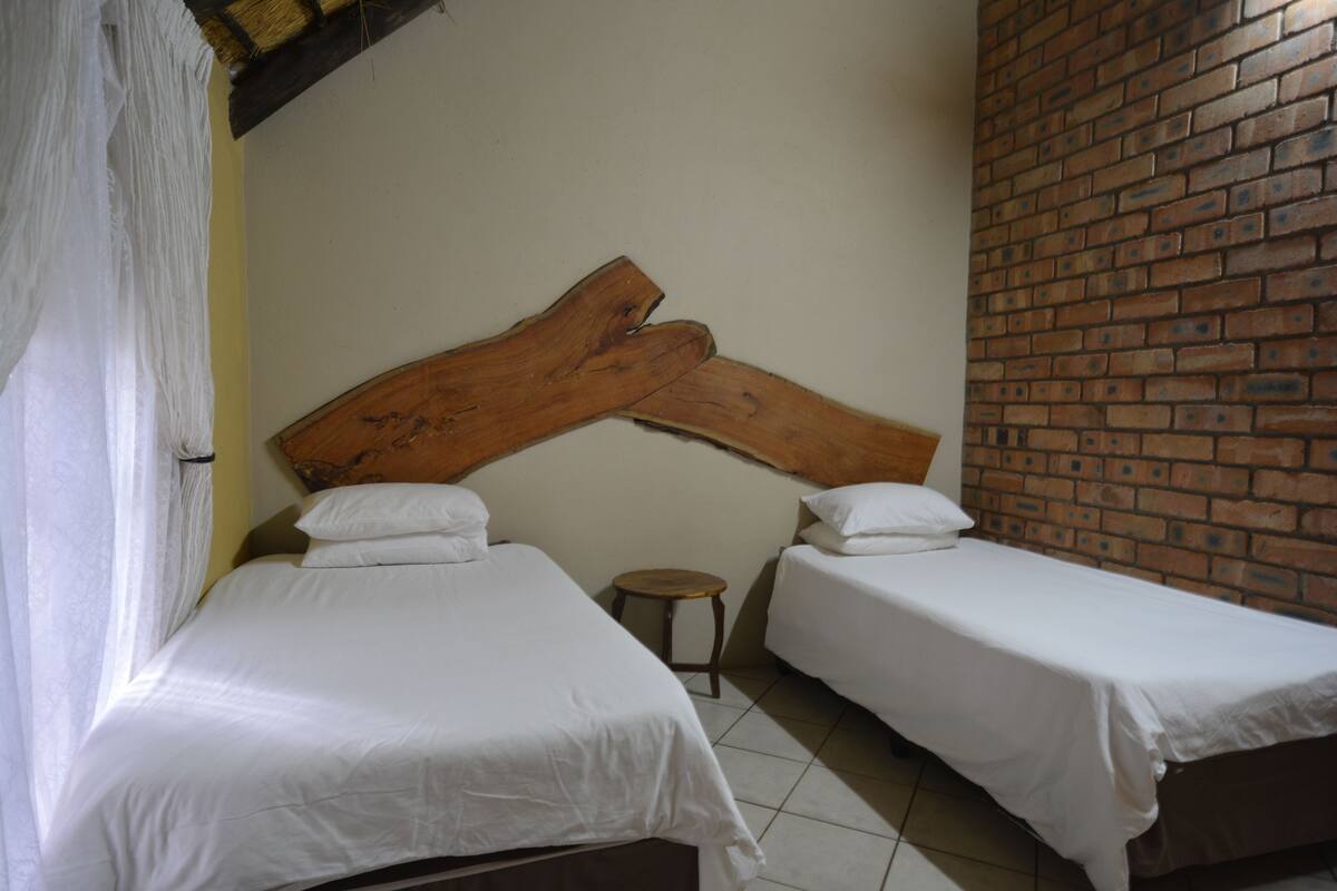 A room with two beds, a wooden headboard, a small stool, and a brick wall.
