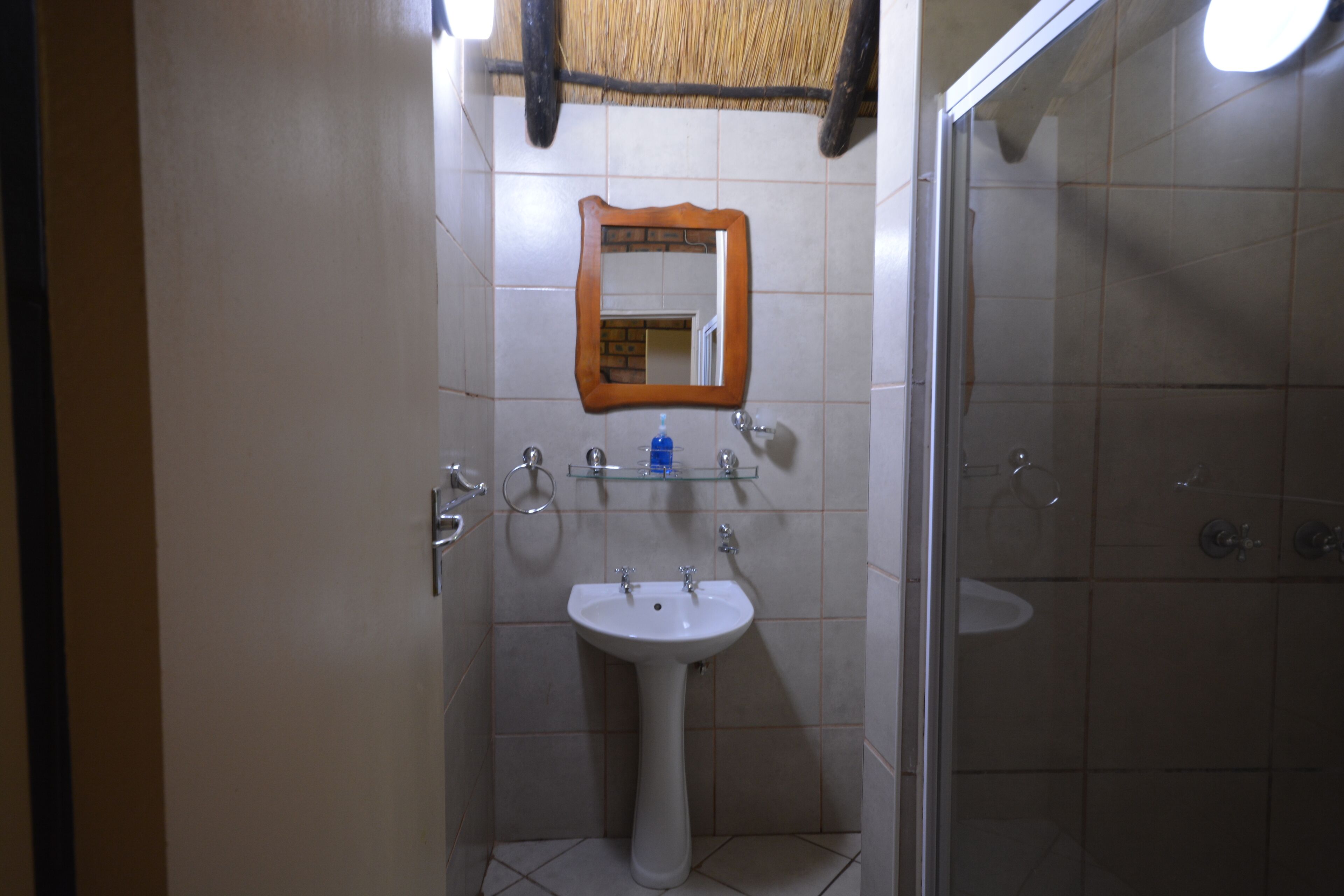 A bathroom with a pedestal sink, a mirror, and a glass shower enclosure.