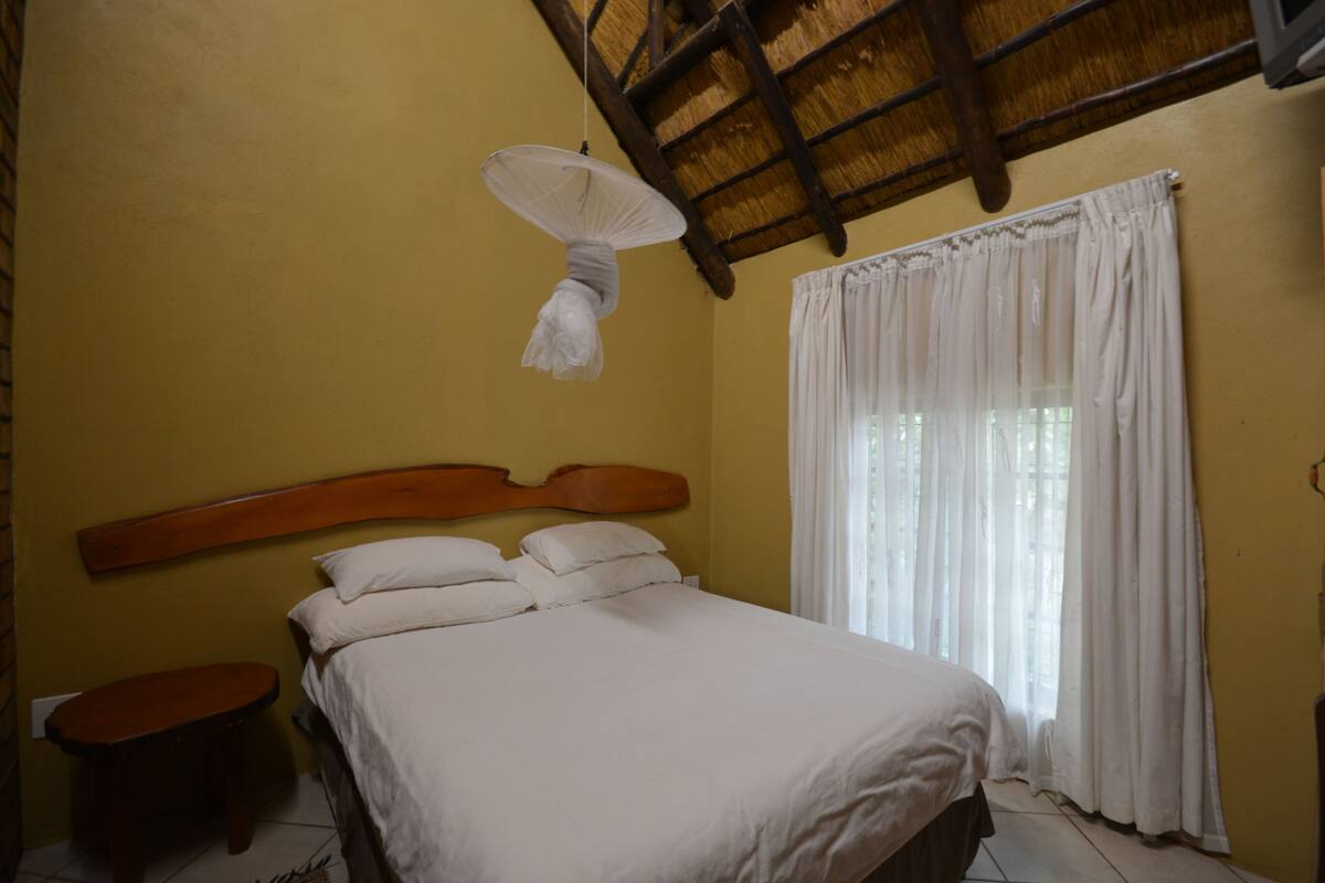 A bedroom with a wooden headboard, a single bed with white linens, a small wooden nightstand, and a hanging light fixture.