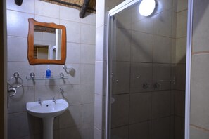 Bathroom features a pedestal sink, mirror, and glass shelves for toiletries, alongside a glass-enclosed shower.