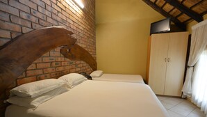 A room with a brick wall, a wooden arch, a bed with white bedding, a wardrobe, and a television on the wall. - Mukurumanzi Lodge (Polokwane)