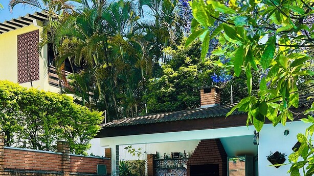A swimming pool with a tiled deck, surrounded by a brick wall and lush greenery. - Casa de Alto Padrão no Jd Marajoara (São Paulo)