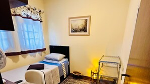 A compact room with a bed, a desk, a chair, a small rug, a picture on the wall, and a window with curtains. - Casa de Alto Padrão no Jd Marajoara (São Paulo)