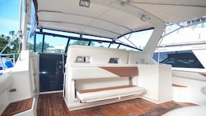 A boat's interior with a wooden deck, a cushioned seating area, and a control panel.