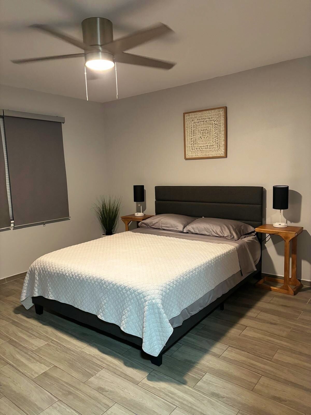 Une chambre à coucher comprenant un lit, un ventilateur de plafond, des lampes de chevet et une œuvre d’art accrochée au mur.
