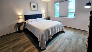 Ein Schlafzimmer mit einem Bett, zwei Nachttischlampen, einem Deckenventilator, einem Fenster mit Jalousien und einem gerahmten Bild an der Wand.