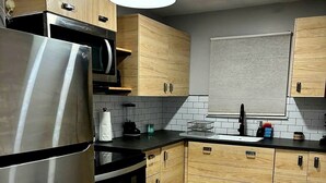 Eine moderne Küche mit Holzausstattung, einem Edelstahlkühlschrank, einer schwarzen Arbeitsplatte und einer schwarzen Pendelleuchte.