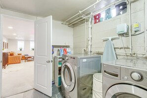Een wasruimte met twee wasmachines, een wandwaterverwarmer en een deur naar een woonkamer.