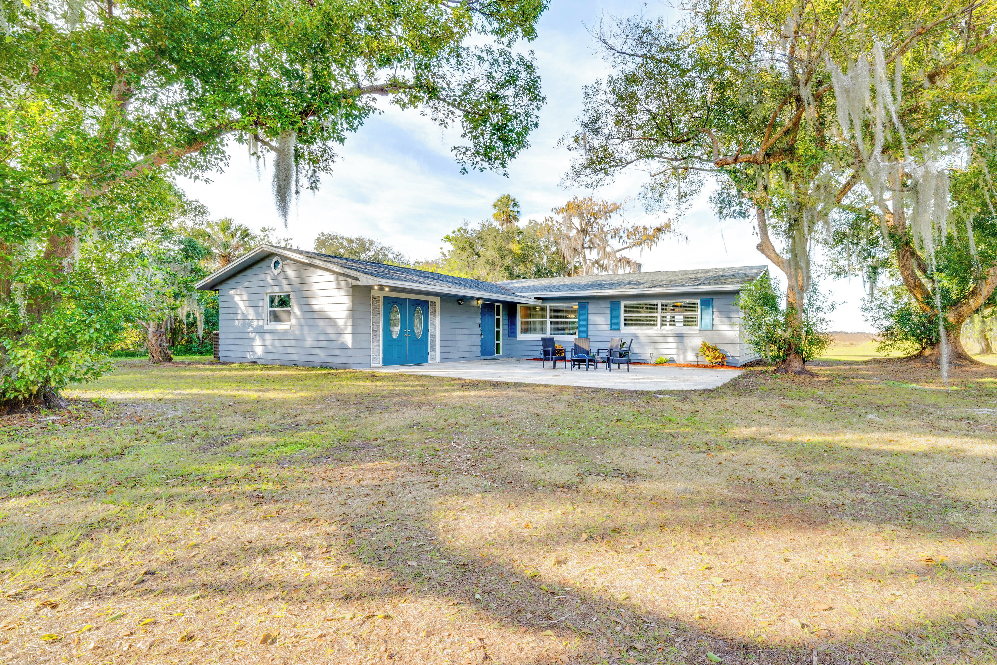 A single-story house with a blue door and windows, surrounded by trees and a grassy yard.