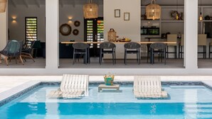 Ein moderner Poolbereich mit Liegestühlen und einer Bar, die durch die Glaswände erkennbar ist.