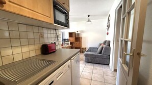 Een praktische keuken met een magnetron, broodrooster en vaatwasser. Een grijze bank en een kleine tafel staan in de woonkamer.