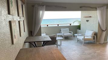 Un balcón con vista al mar, amoblado con sillas y una mesa blancos.