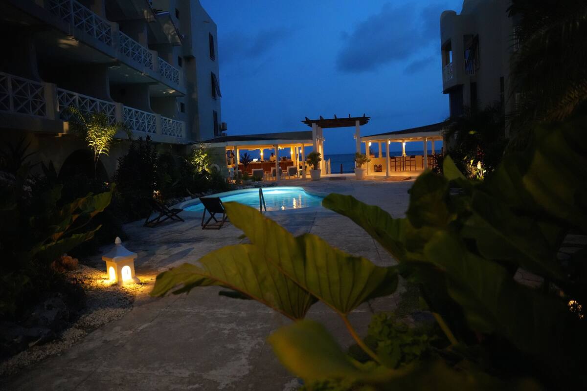 Ein Poolbereich mit Liegestühlen und einer Pergola, umgeben von Gebäuden mit Balkonen und Außenbereich.