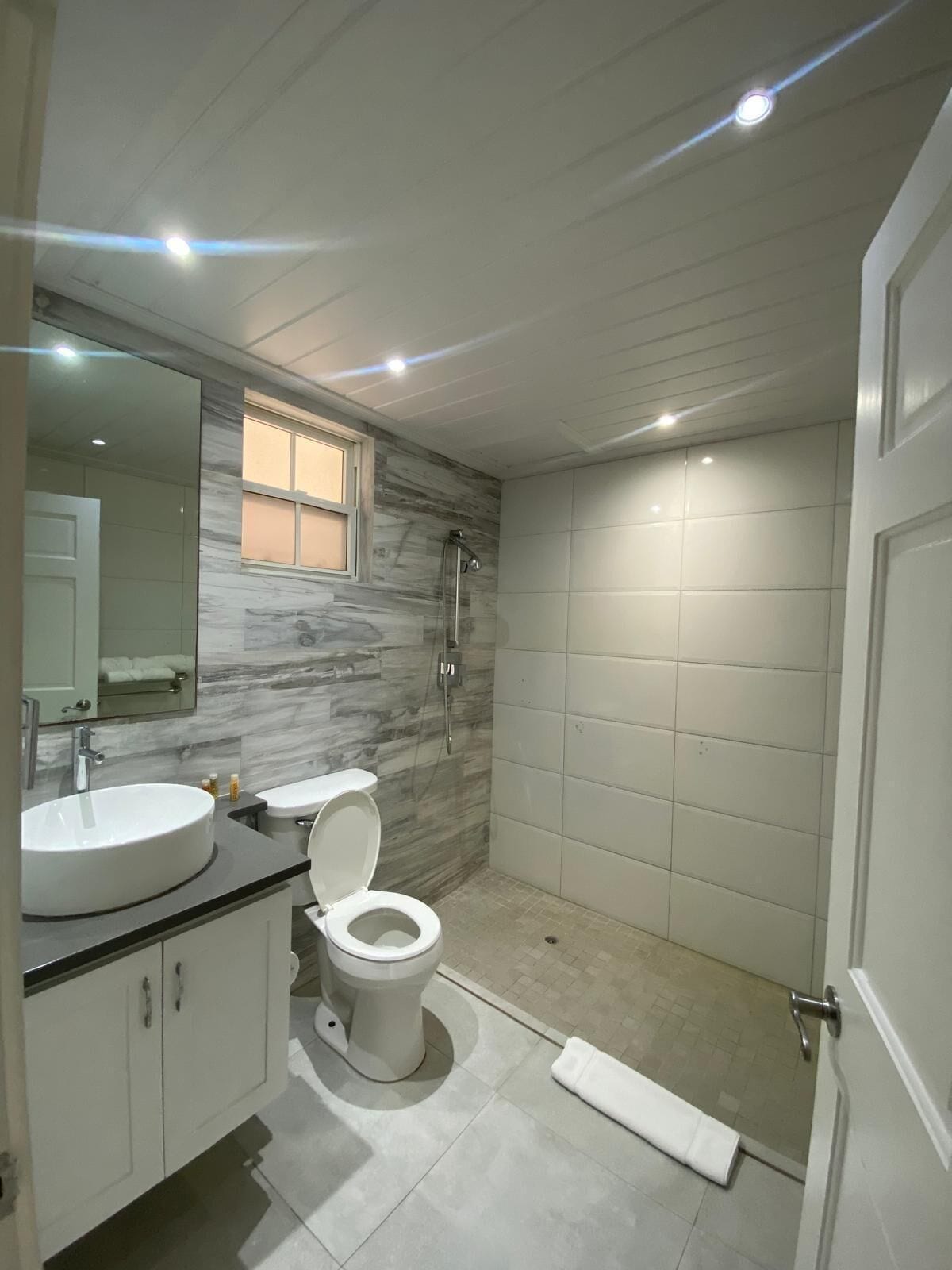 A modern bathroom with a marble backsplash, a white toilet, a sink, and a shower.
