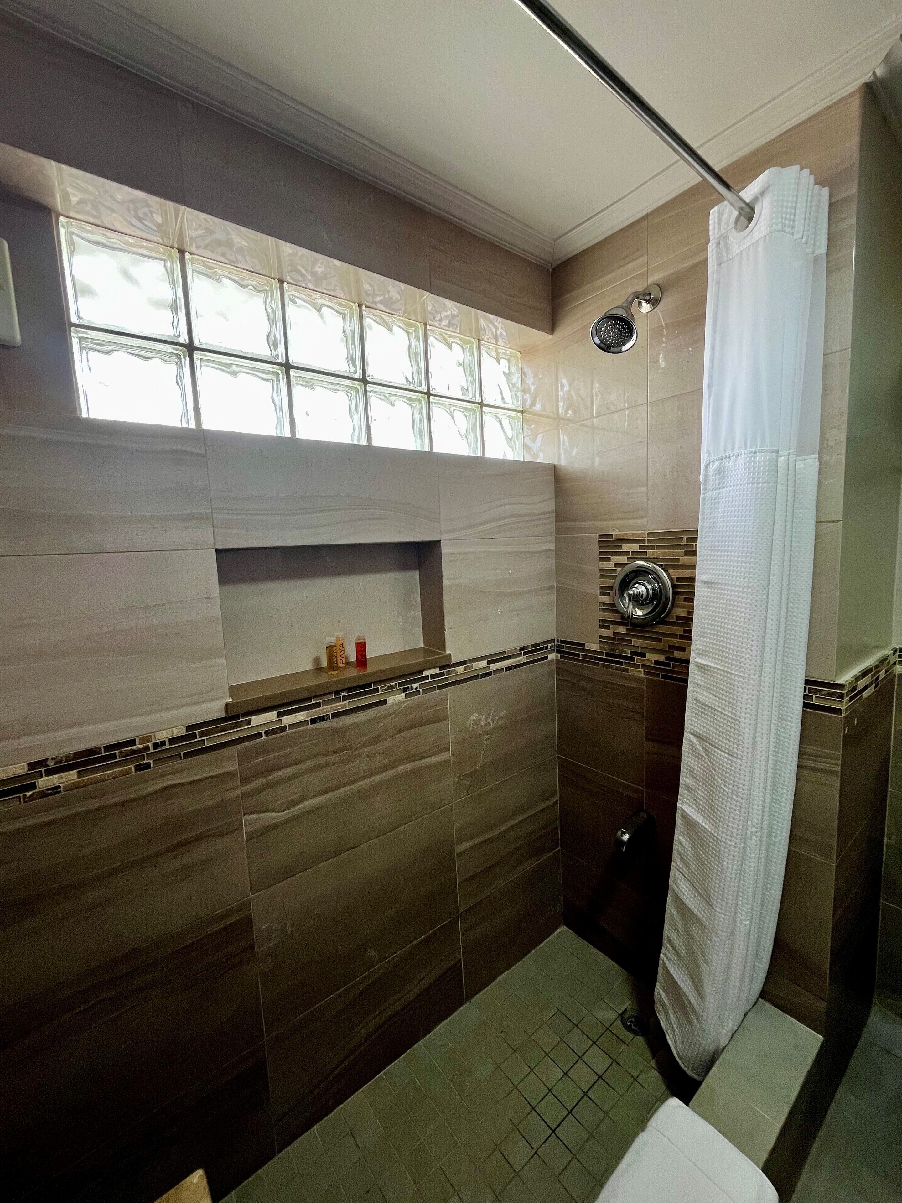 Un bagno con doccia, una finestra vista e uno scaffale con articoli da toilette.
