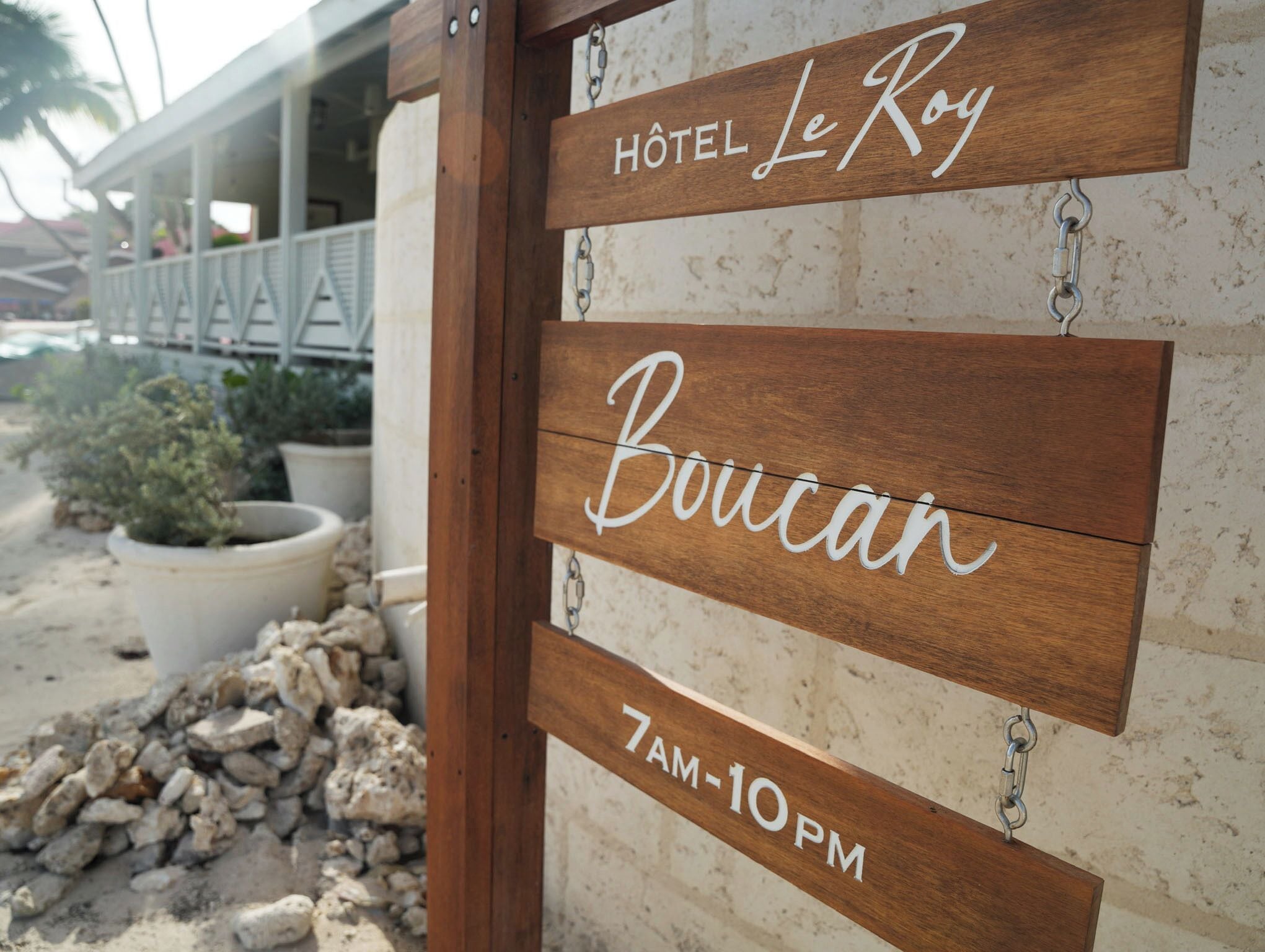 A wooden sign with 'Hôtel Le Roy' and 'Boucan 7AM-10PM' indicating the hotel name and operating hours.