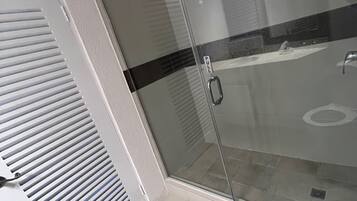 A bathroom with a glass shower door, a white vent, and a black stripe on the wall.