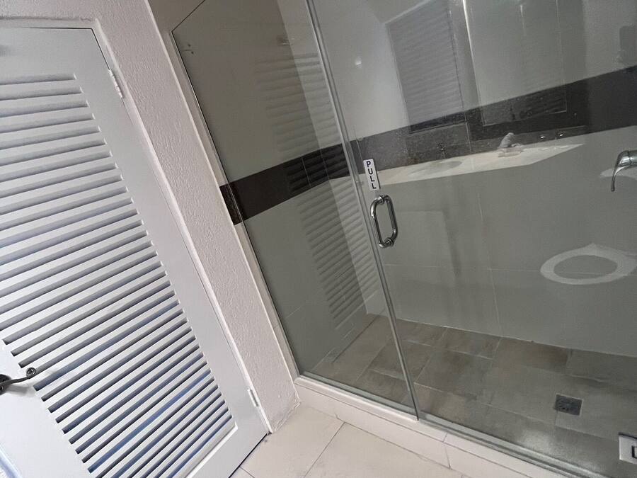 A bathroom with a glass shower door, a white vent, and a black stripe on the wall.