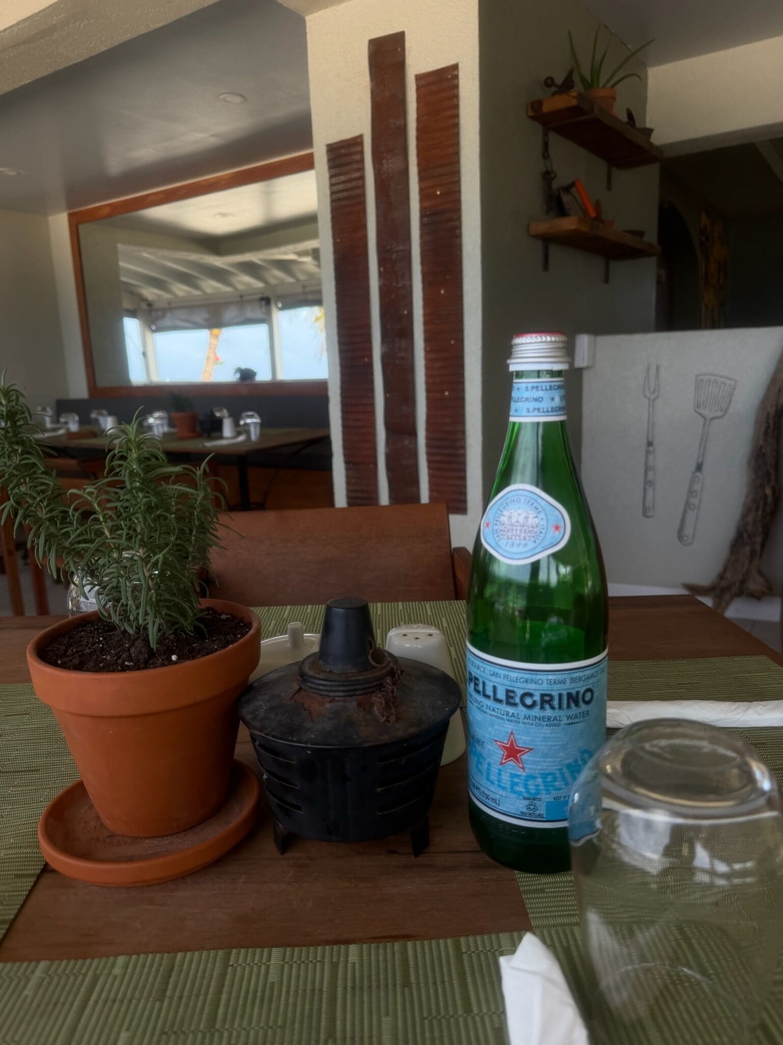 Una mesa con una botella de agua Pellegrino, una planta en maceta, un recipiente pequeño negro y un tarro de vidrio.