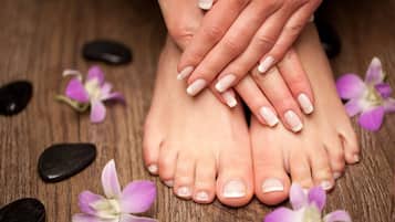Une paire de pieds aux ongles parfaitement manucurés, reposant sur une surface en bois, entourée de pierres et de fleurs violettes.