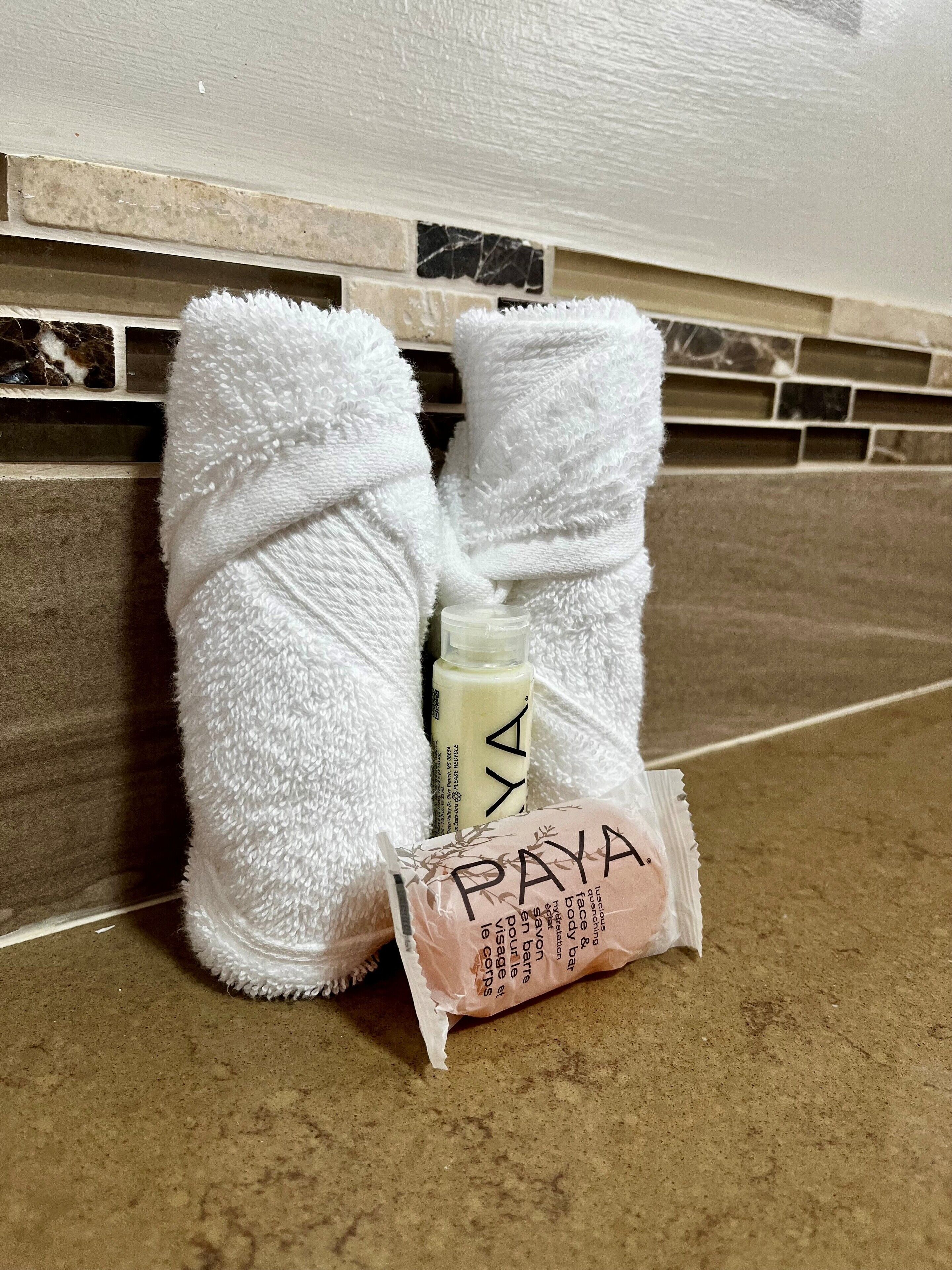 Un baño con un perchero que sostiene dos toallas blancas, una botella de loción y una pastilla de jabón.