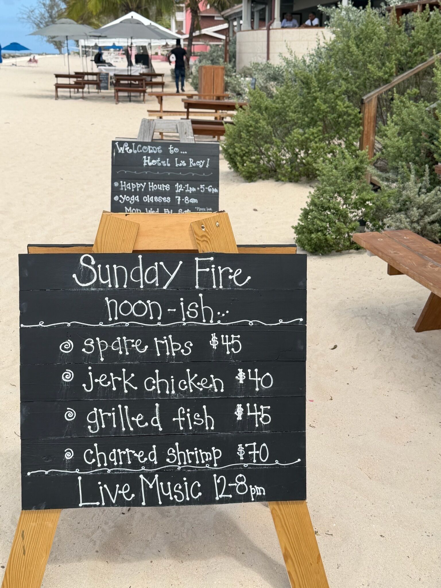 Tabla de menú de un restaurante frente a la playa, con platos como pescado a la parrilla y pollo al estilo jerk.