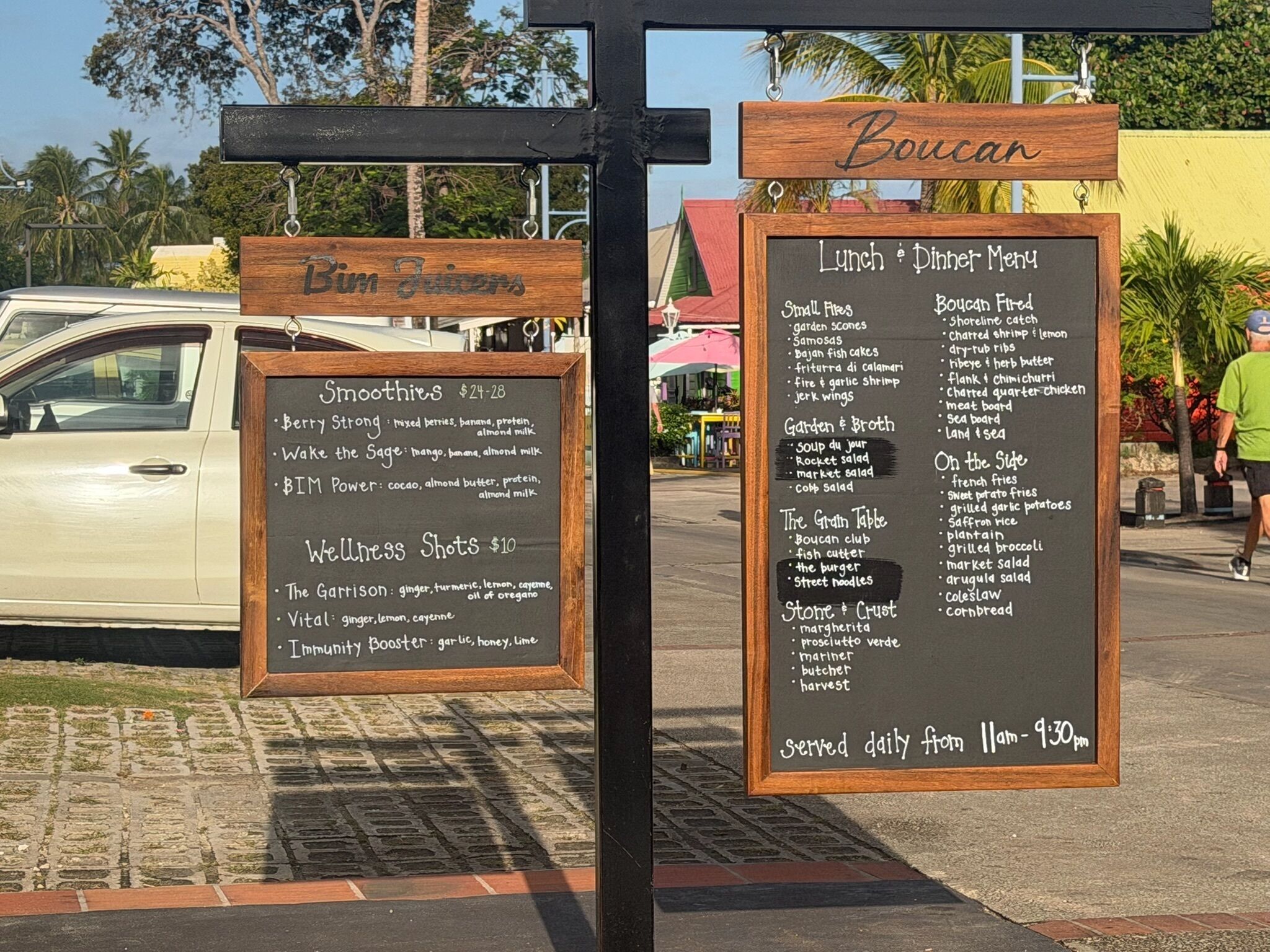 A menu board with a list of food items and prices, a sign for 'Boucan,' and a car parked nearby.