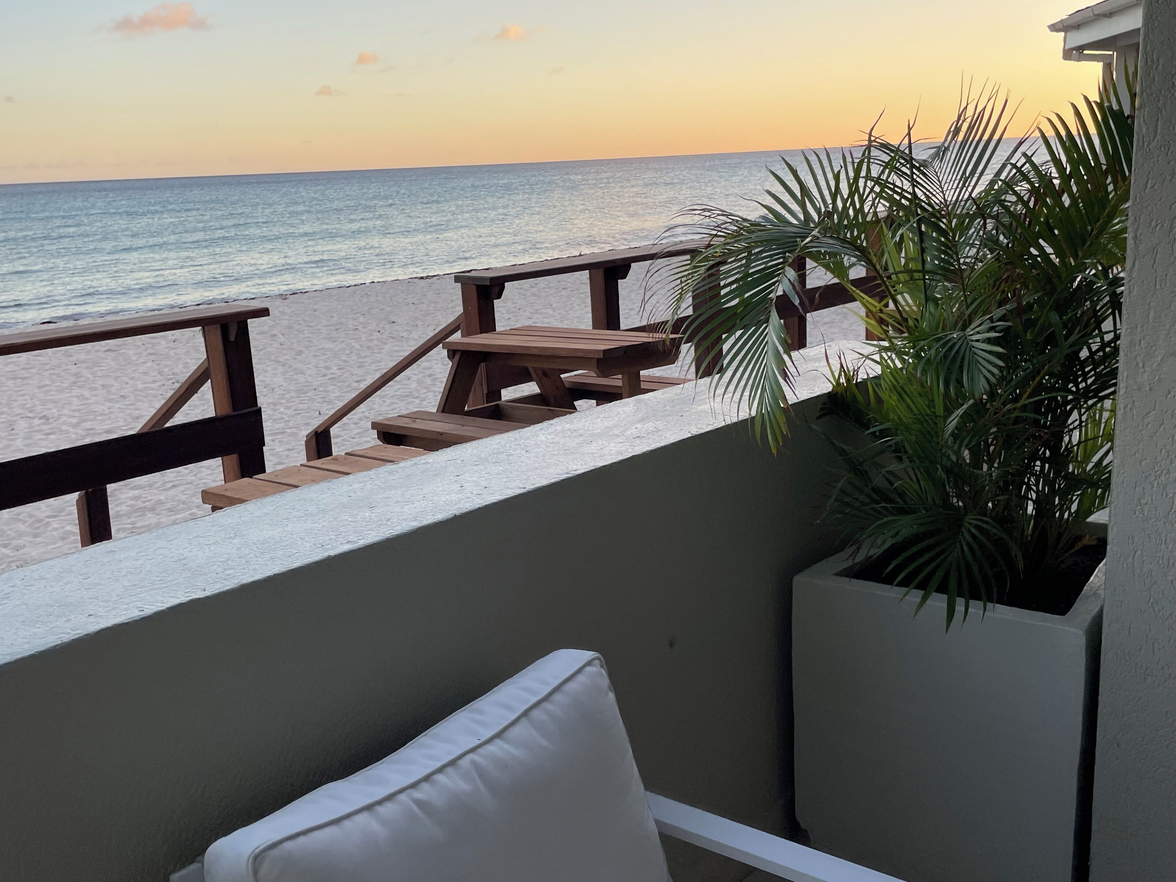 A balcony with a view of the beach and ocean at sunset.