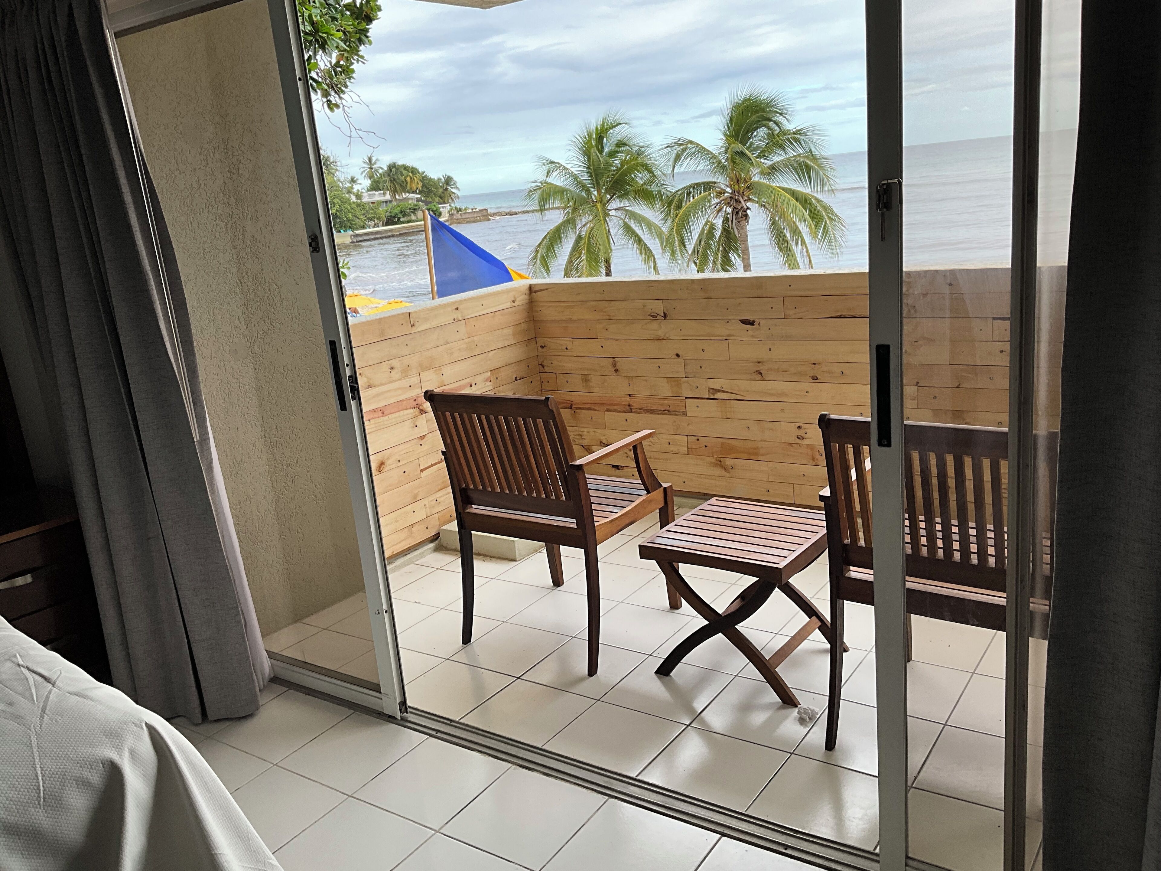 Un balcón con muebles de madera, vista al océano y palmeras.