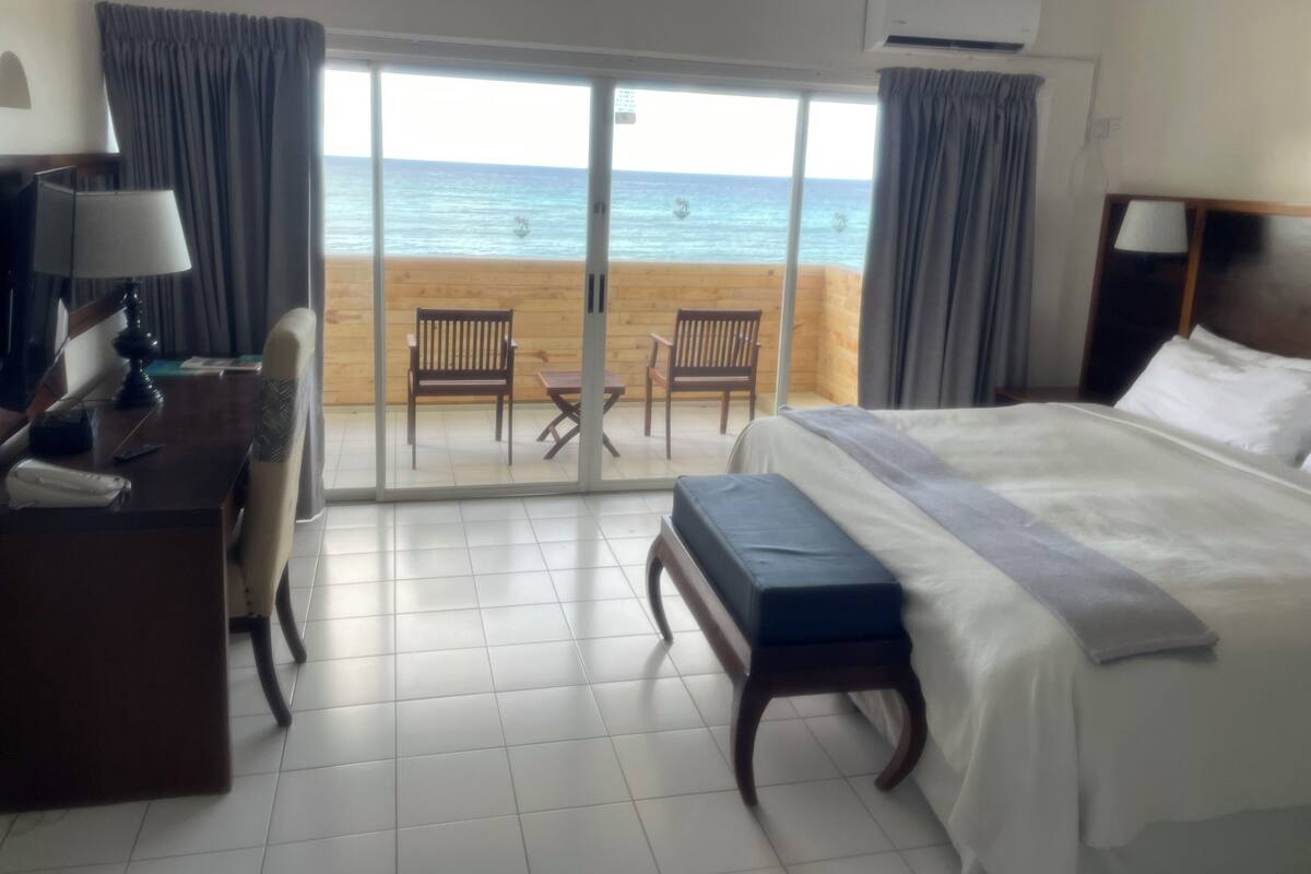 Ein Hotelzimmer mit Bett, Schreibtisch, Stuhl und Blick auf Strand und Meer.
