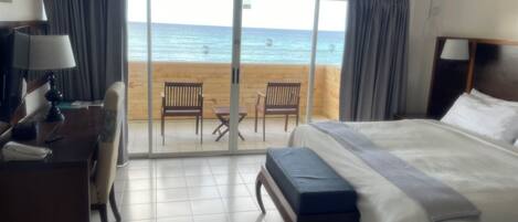 A hotel room with a bed, a desk, a chair, and a view of the beach and ocean.
