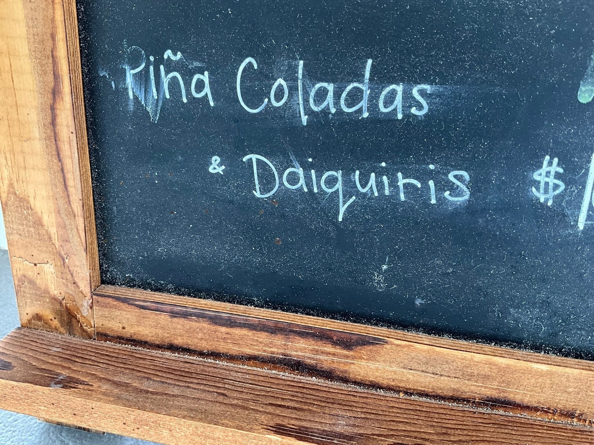 A chalkboard with 'Riña Coladas & Daiquiris' written on it, indicating a menu or list of items.