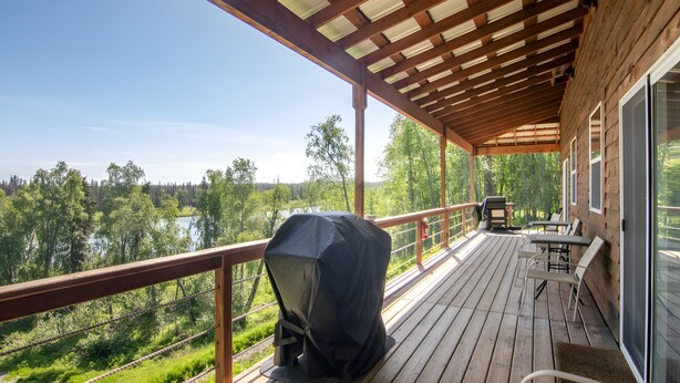 A covered deck with a grill, outdoor seating, and a view of a lake and forest. - Kenai River Views & Access: Soldotna Apartment! (Soldotna)