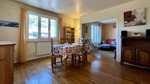 Comedor con una mesa para cuatro, suelo de madera, un radiador y una ventana con cortinas.