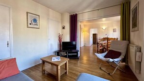 Una sala de estar con un sofá, una mesita, un televisor sobre un mueble bajo y una silla.
