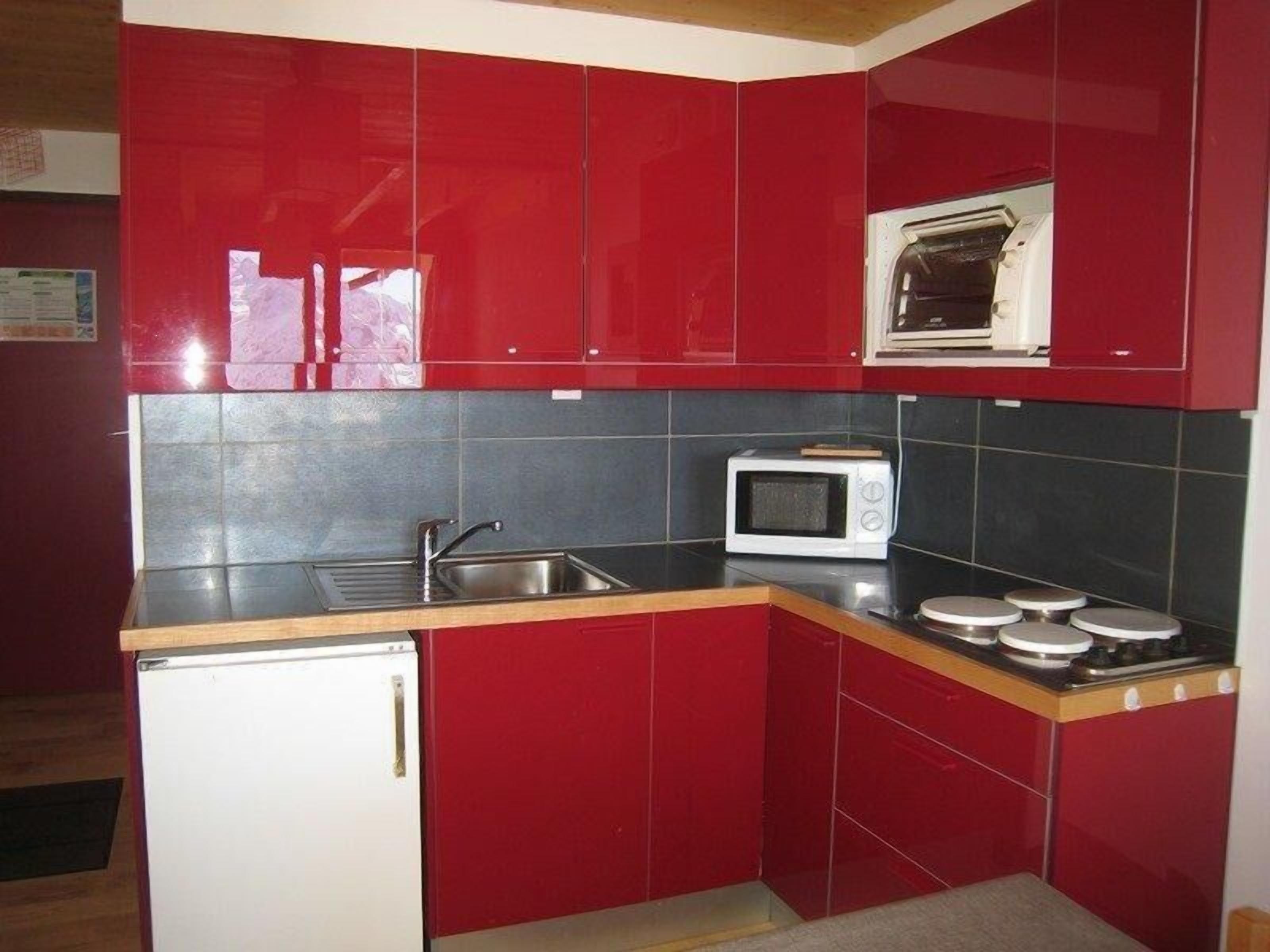 A compact kitchen with red cabinets, a microwave, a sink, and a small refrigerator.