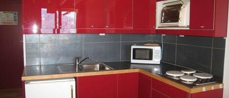 A compact kitchen with red cabinets, a microwave, a sink, and a small refrigerator.