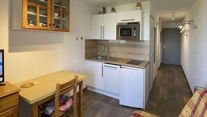 Kompakti keittiö, jossa on mikroaaltouuni, pesuallas ja kaappeja. Olohuoneessa on ruokapöytä tuoleineen sekä sohva.