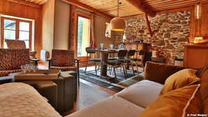 Una habitación acogedora con vigas de madera, una pared de piedra, una zona de comedor con sillas y un sofá con cojines.